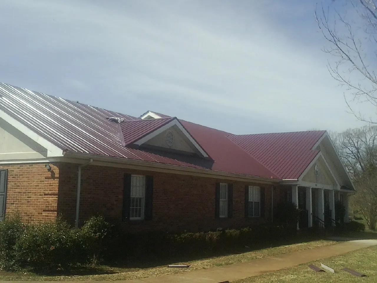 Red metal roof with gabled entries on a long brick building, from a Hail Damage Roof Repair job in Ashville