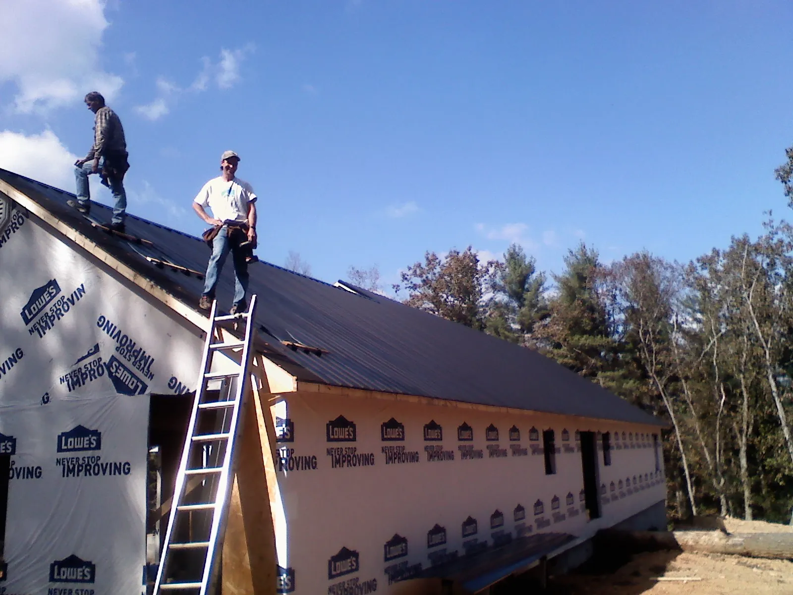 Two roofers standing on a long dark metal roof over a wrapped building in Ashville