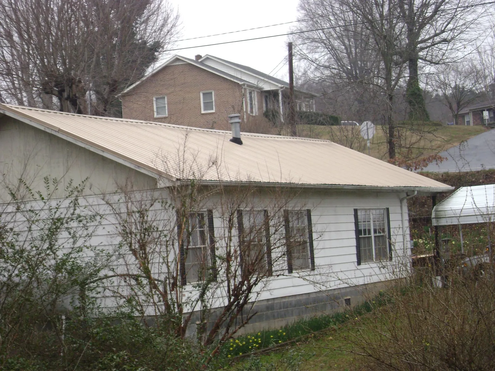 Tan metal roof on a white sided house set into a hillside — Commercial Roofing by Roofing Brothers in Ashville